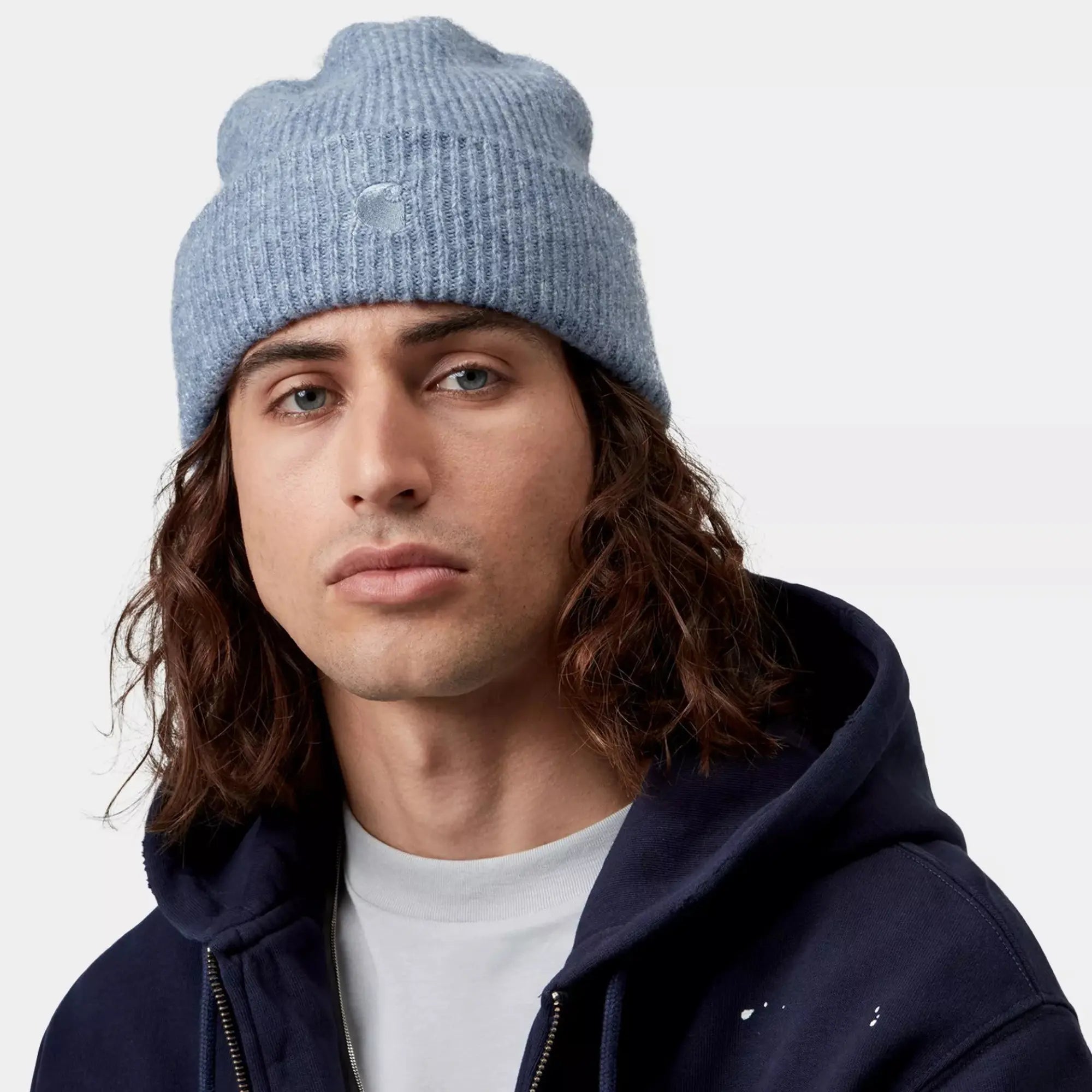 Homme portant le bonnet Curtis Shady Blue Carhartt WIP bleu gris clair, revers relevé, avec un hoodie zippé marine