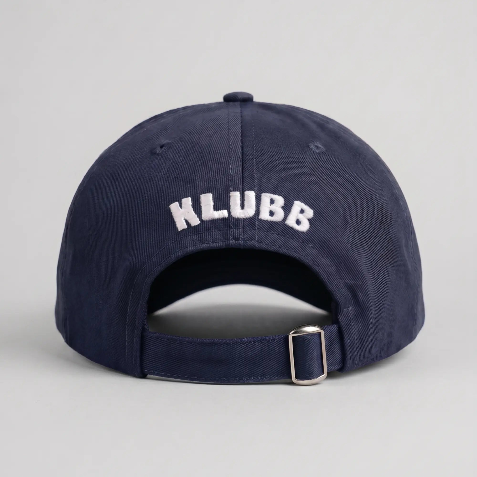 Dos de la casquette Klubb marine : nom KLUBB brodé blanc courbé, ouverture arrière et sangle réglable à boucle argentée