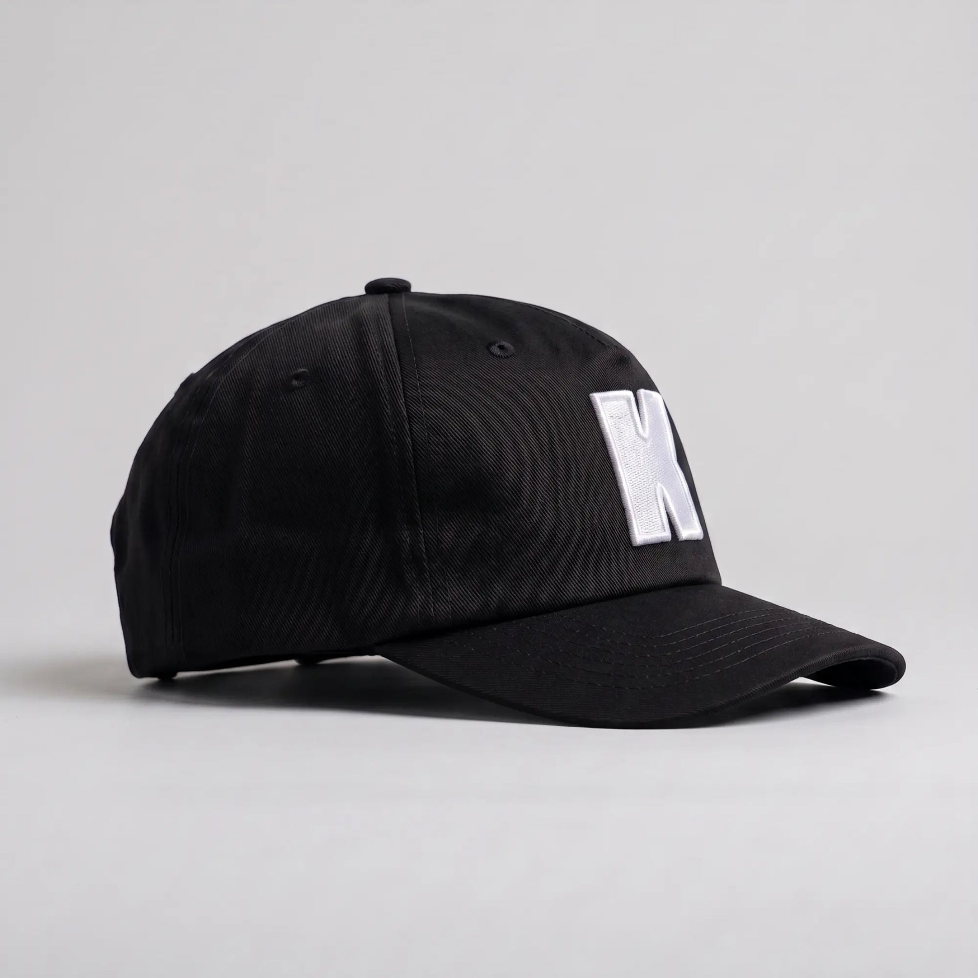 Profil droit de la casquette Klubb noire : calotte 5 panneaux sans renfort avant, visière incurvée, œillets brodés
