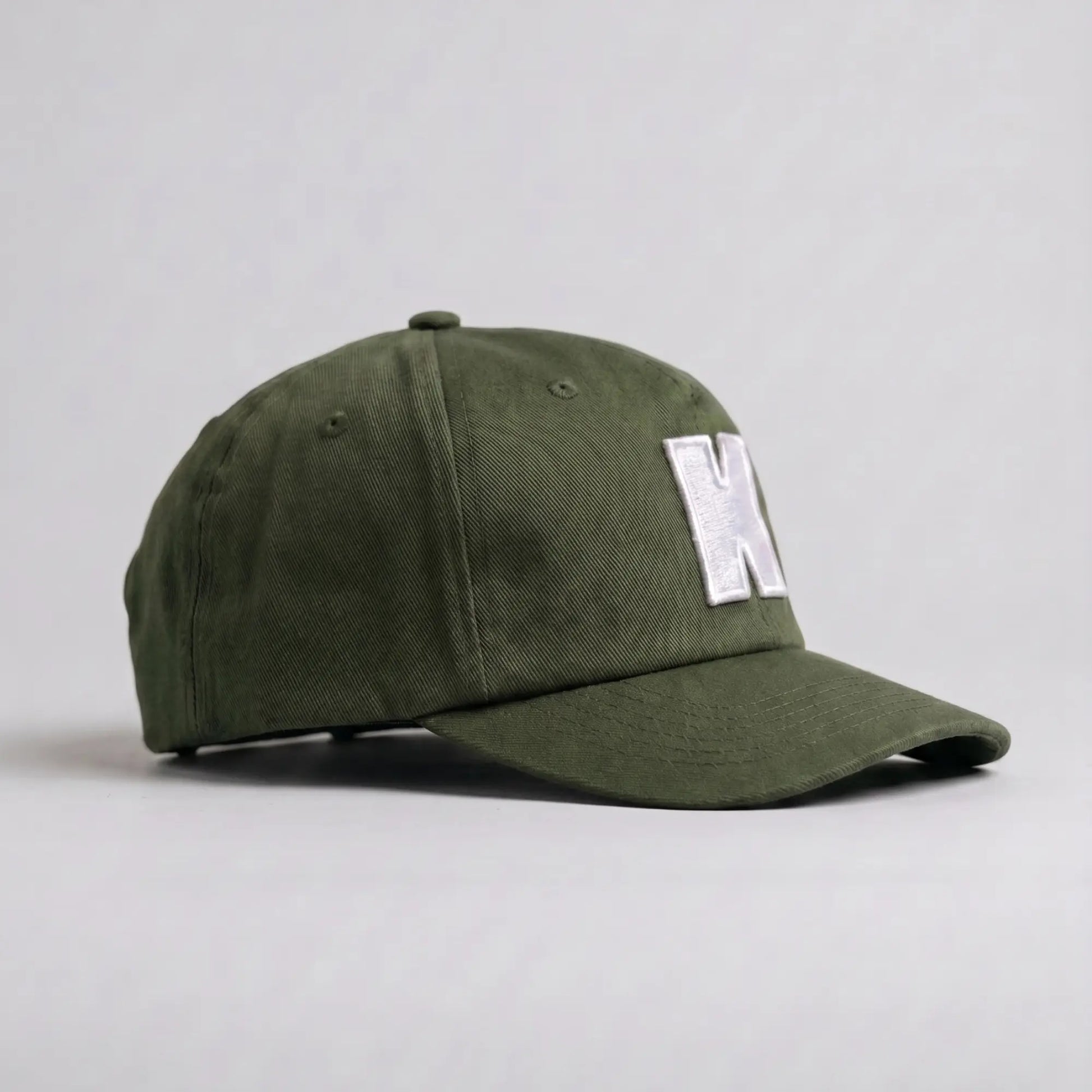 Casquette Klubb vert olive de trois-quarts : couronne basse non rigide, aérations brodées et visière longue surpiquée