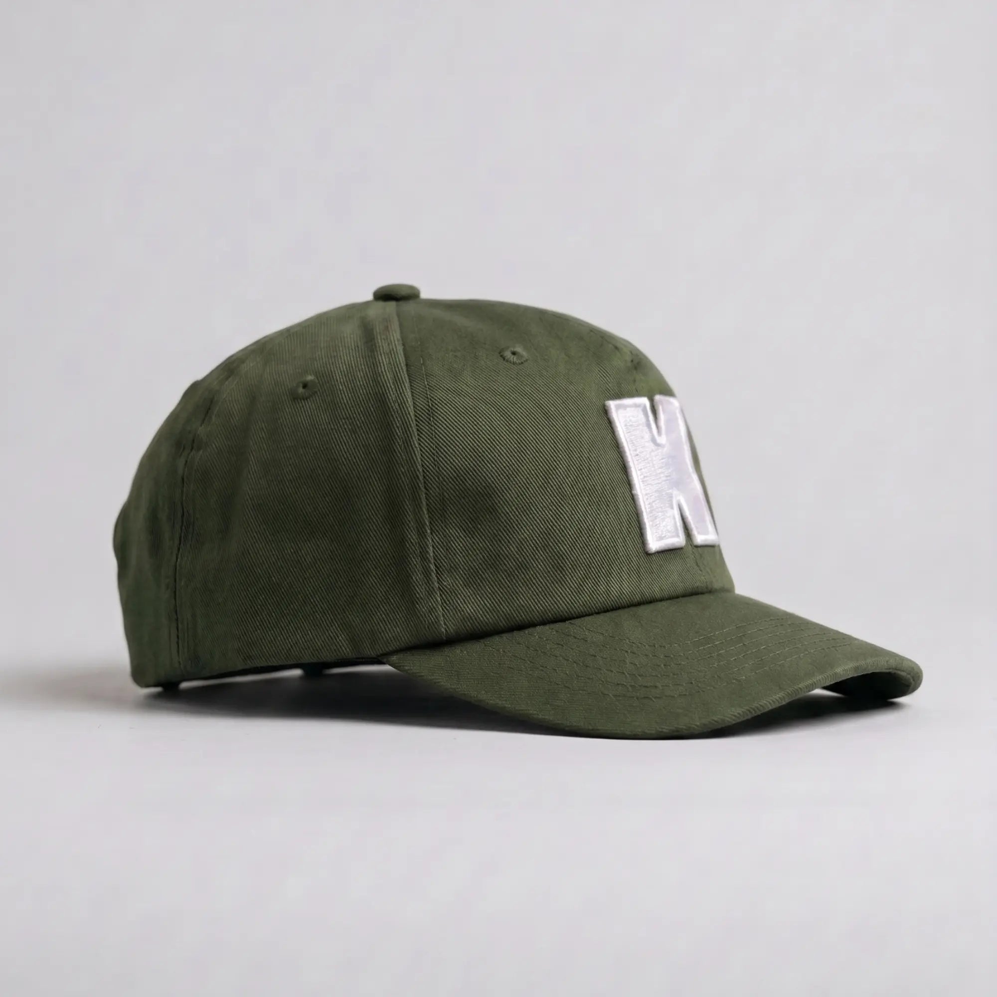 Casquette Klubb vert olive de trois-quarts : couronne basse non rigide, aérations brodées et visière longue surpiquée