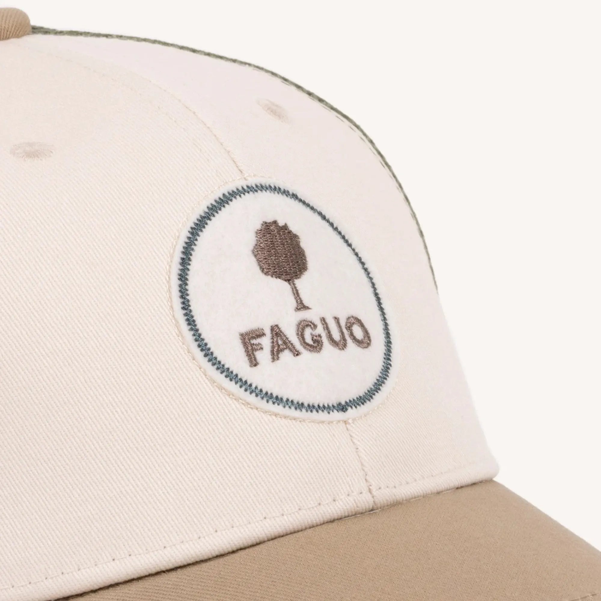 Détail du badge rond brodé Faguo, arbre marron sur feutre écru, casquette trucker beige et vert
