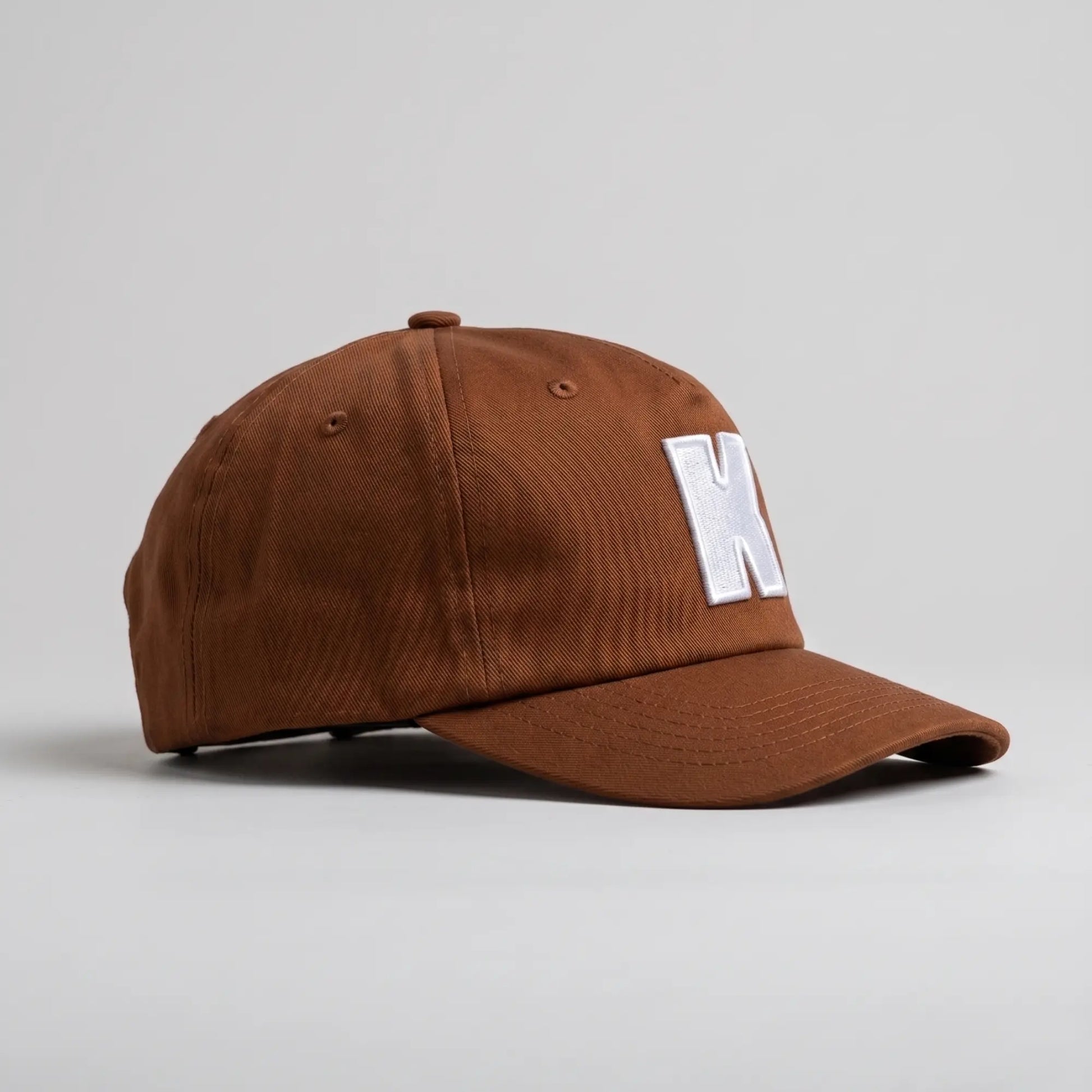 Casquette Klubb marron de profil : calotte non structurée, visière préformée surpiquée et œillets d’aération brodés