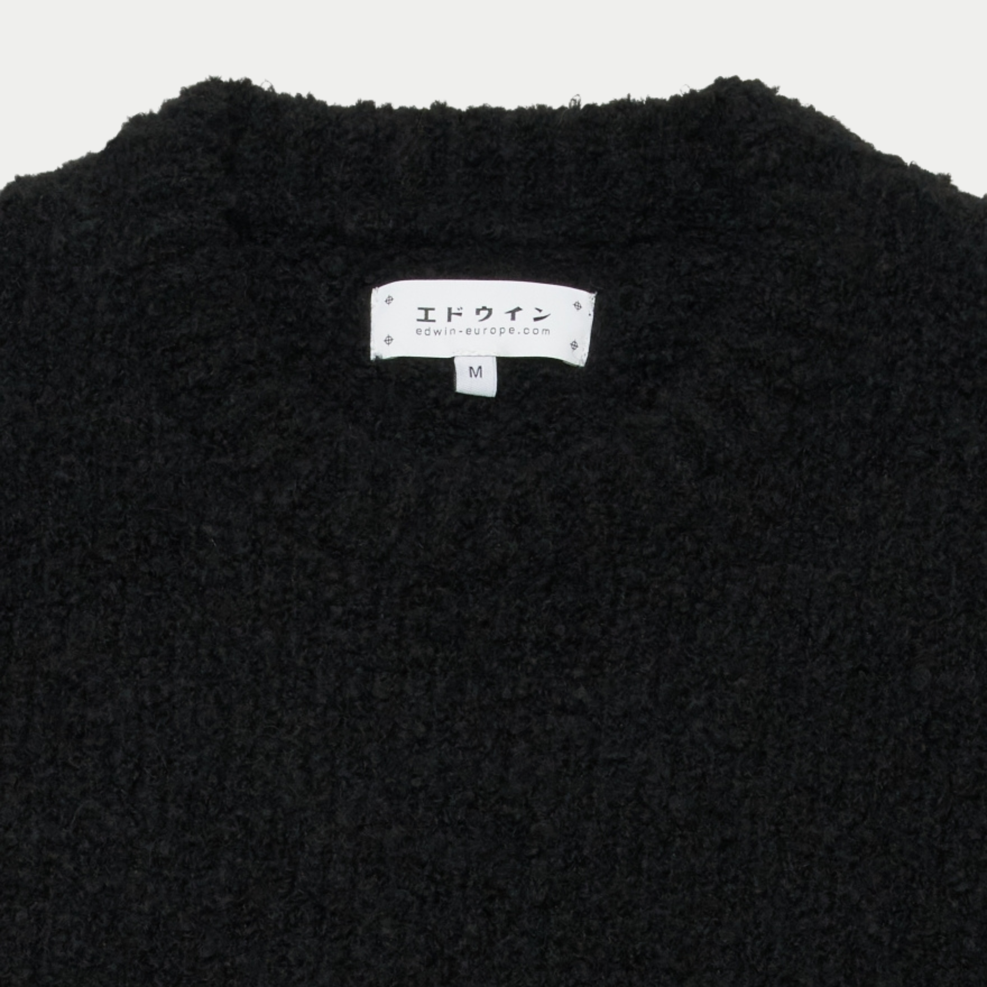Détail du col rond du pull Dun Edwin noir et de son étiquette de marque intérieure