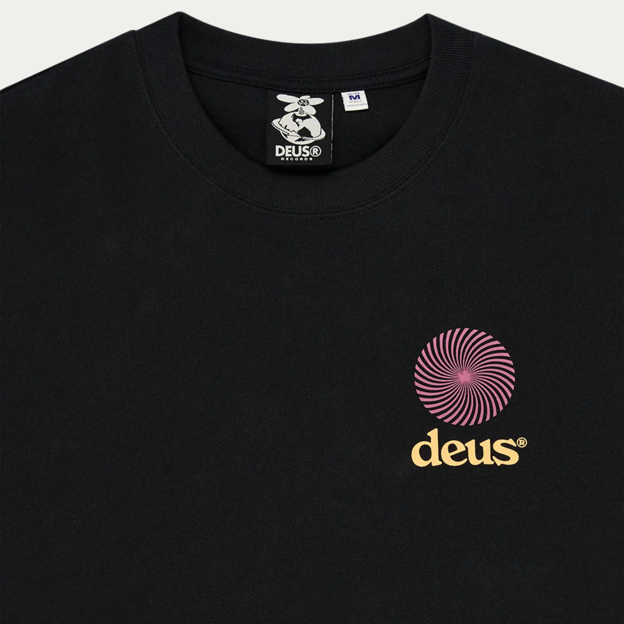 Détail du col du T-shirt Strata noir Deus Ex Machina, étiquette Deus Records et logo spirale sur la poitrine