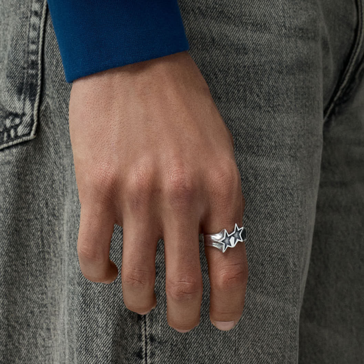 Bague Tilted Icon argentée Twojeys portée à la main, sur un jean gris