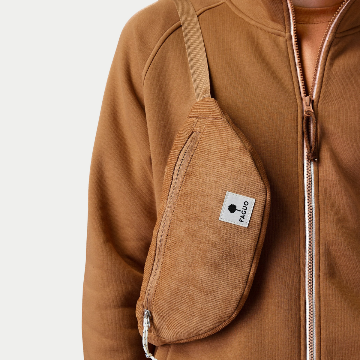 Banane Faguo Cambium camel portée en bandoulière sur une veste zippée marron