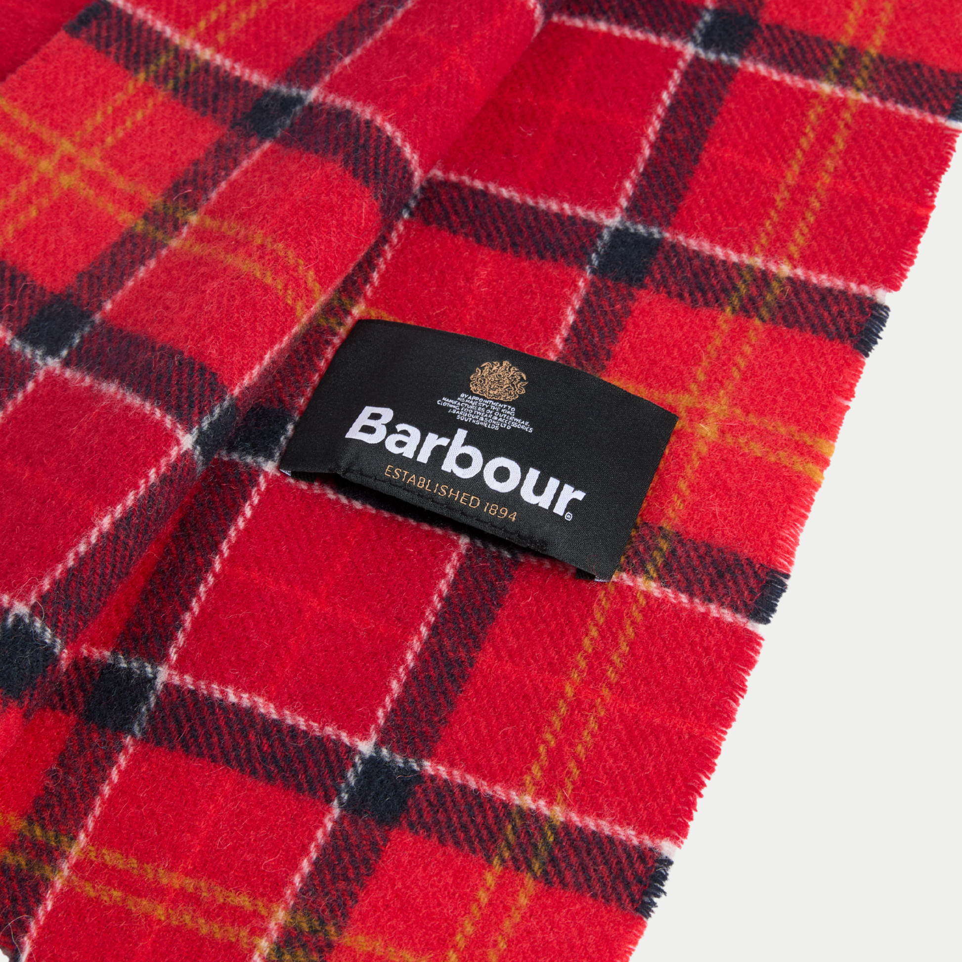 Gros plan sur l'étiquette tissée noire Barbour Established 1894, cousue sur le tartan rouge en laine