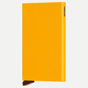Porte-cartes aluminium jaune ocre à texture poudrée, logo gravé sombre sur la tranche