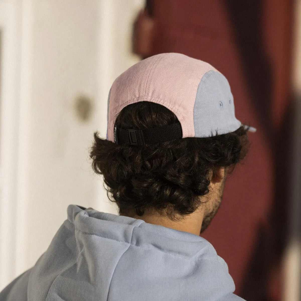 Casquette portée de dos : sangle de serrage noire à boucle, panneaux arrière rose pâle et bleu gris