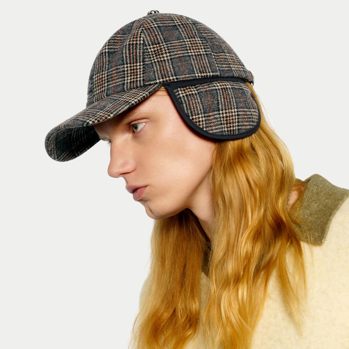 Casquette Kangol à carreaux gris portée de profil, rabat d'oreille rabattu le long de la joue