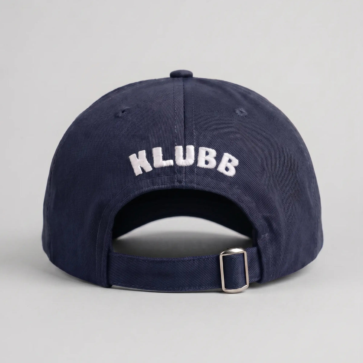 Dos de la casquette Klubb marine : nom KLUBB brodé blanc courbé, ouverture arrière et sangle réglable à boucle argentée