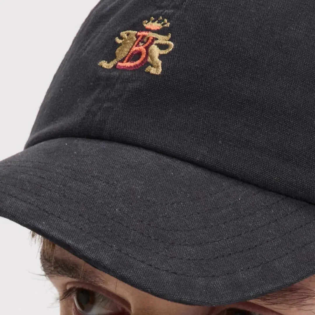 Macro portée : visière surpiquée et blason brodé fil doré et rouge sur le coton noir