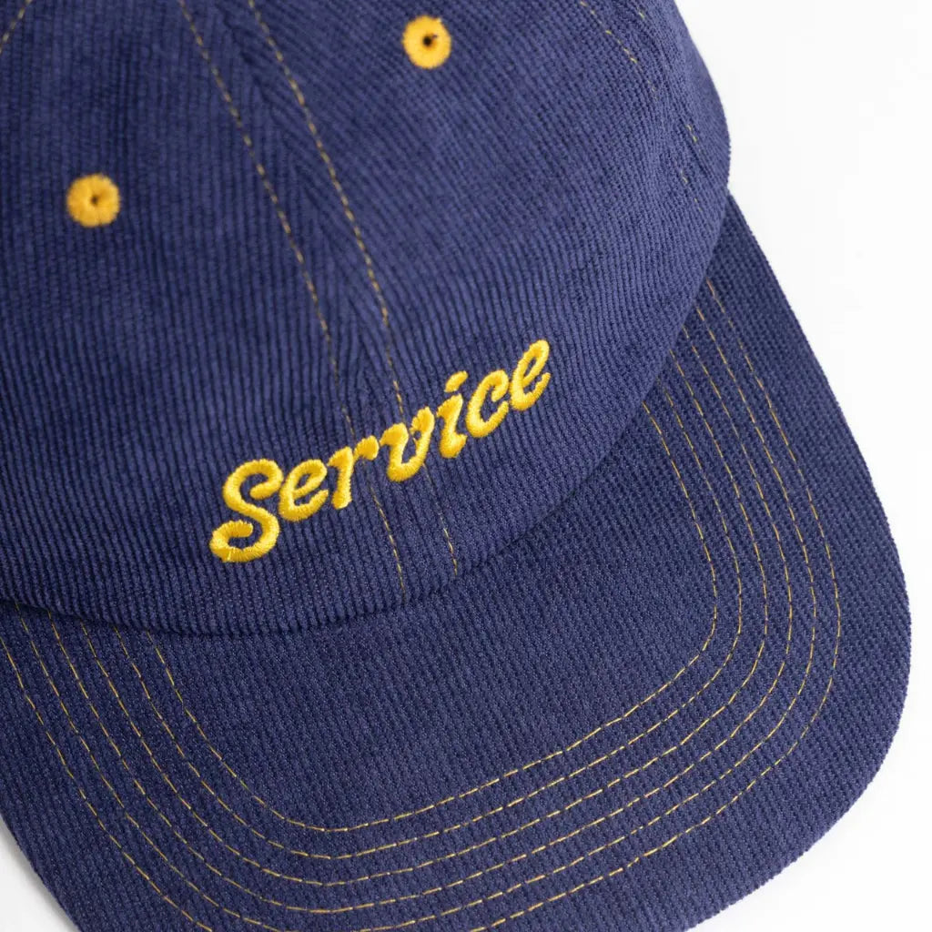 Gros plan de la broderie script jaune Service et des fines côtes du velours sur la visière
