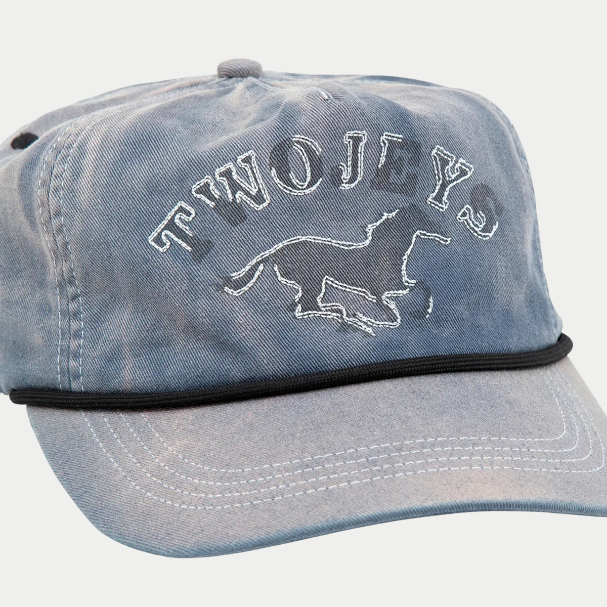 Gros plan sur la broderie cheval TWOJEYS et les surpiqûres écrues de la casquette délavée bleue