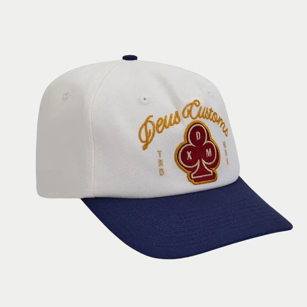 Casquette Basto Deus Ex Machina écrue à visière marine, écusson trèfle rouge et script doré, vue trois quarts