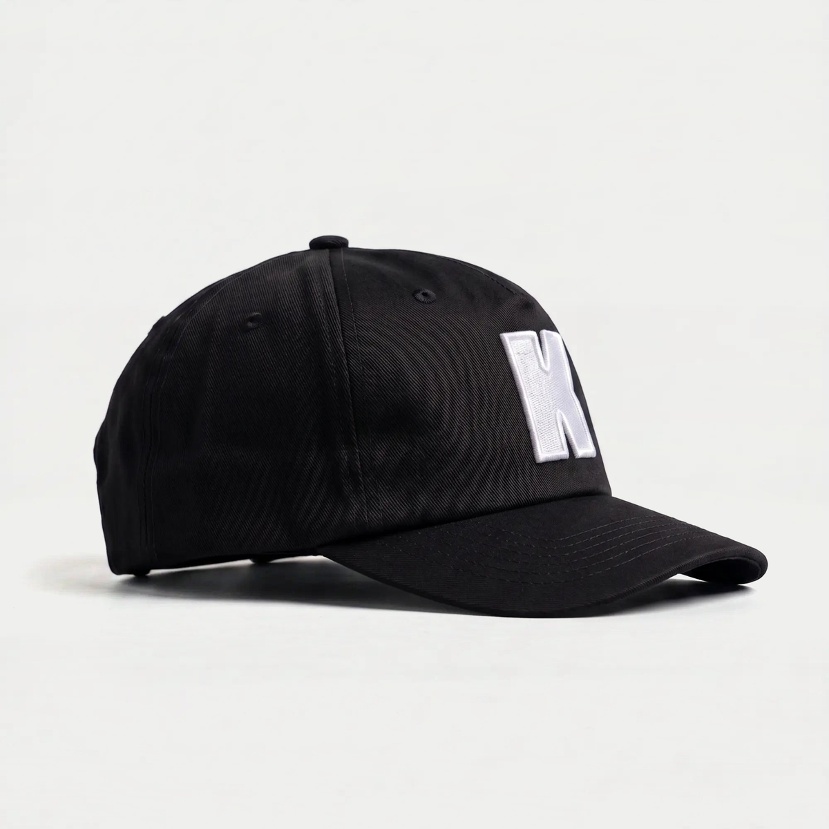 Profil droit de la casquette Klubb noire : calotte 5 panneaux sans renfort avant, visière incurvée, œillets brodés