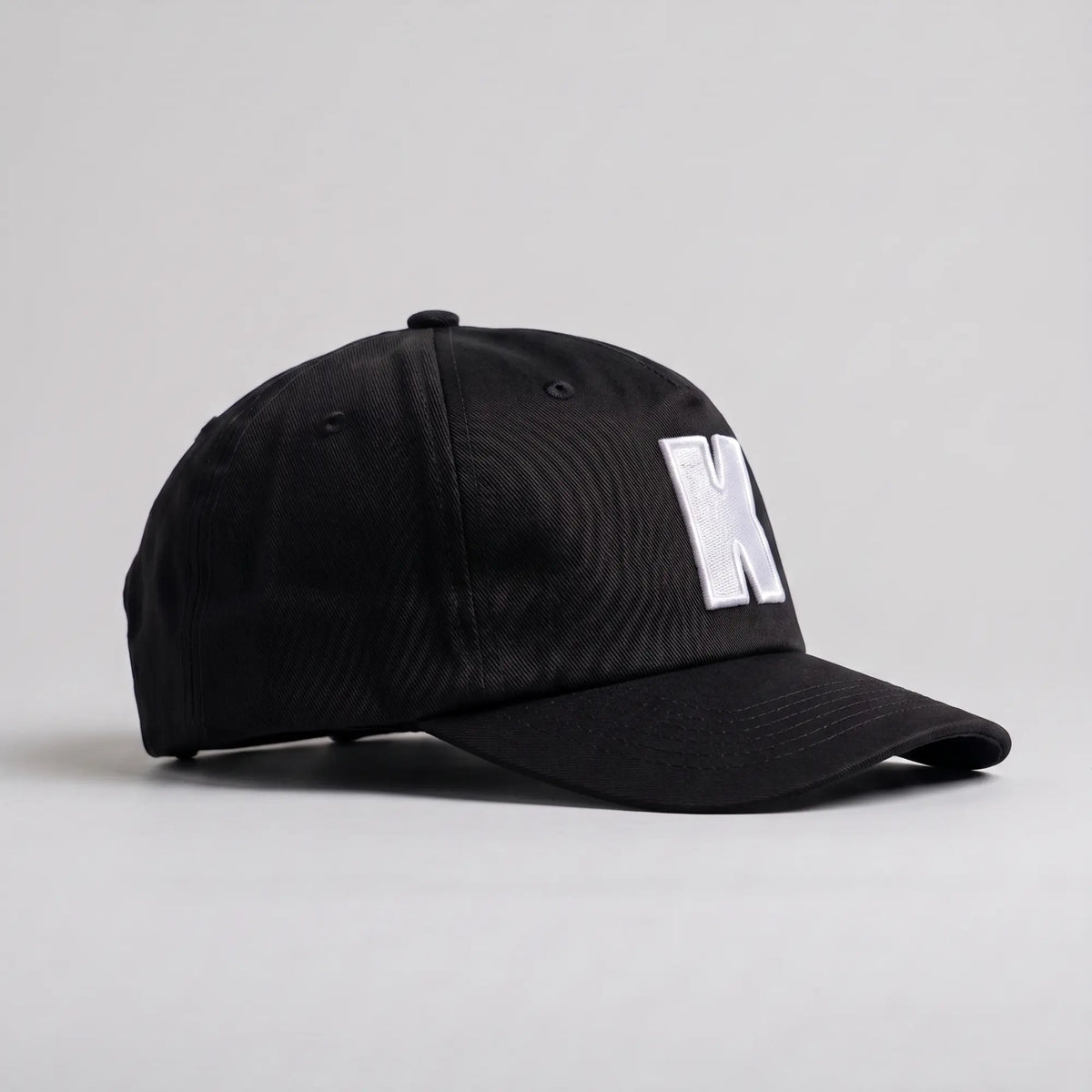 Profil droit de la casquette Klubb noire : calotte 5 panneaux sans renfort avant, visière incurvée, œillets brodés