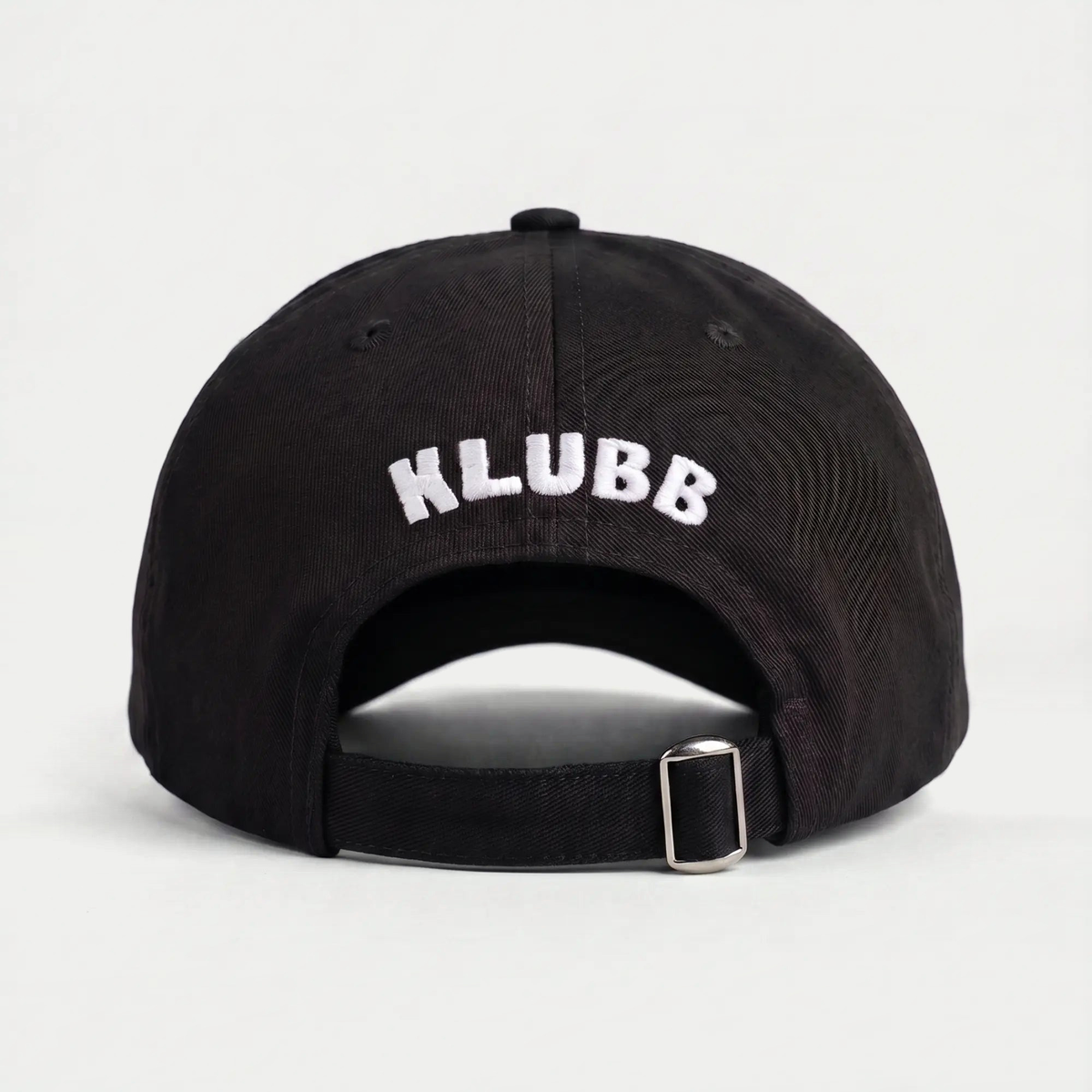 Dos de la casquette Klubb noire : lettrage KLUBB blanc brodé en arc au-dessus de la sangle et de sa boucle métal
