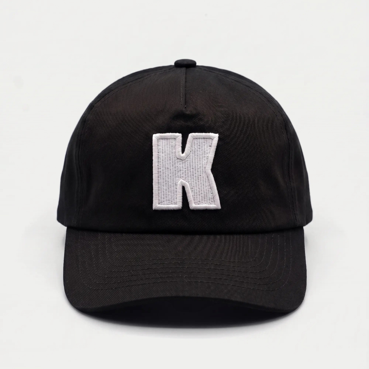 Vue de face de la casquette Klubb noire : K blanc brodé se détachant en fort contraste sur le sergé de coton noir
