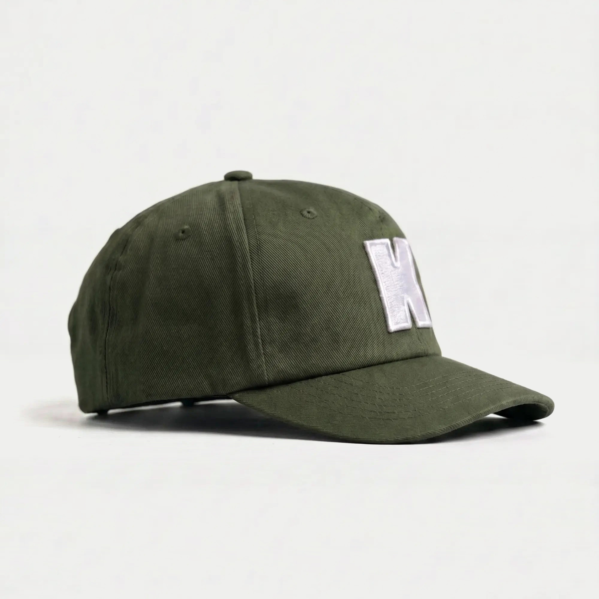Casquette Klubb vert olive de trois-quarts : couronne basse et souple, aérations brodées et visière longue surpiquée
