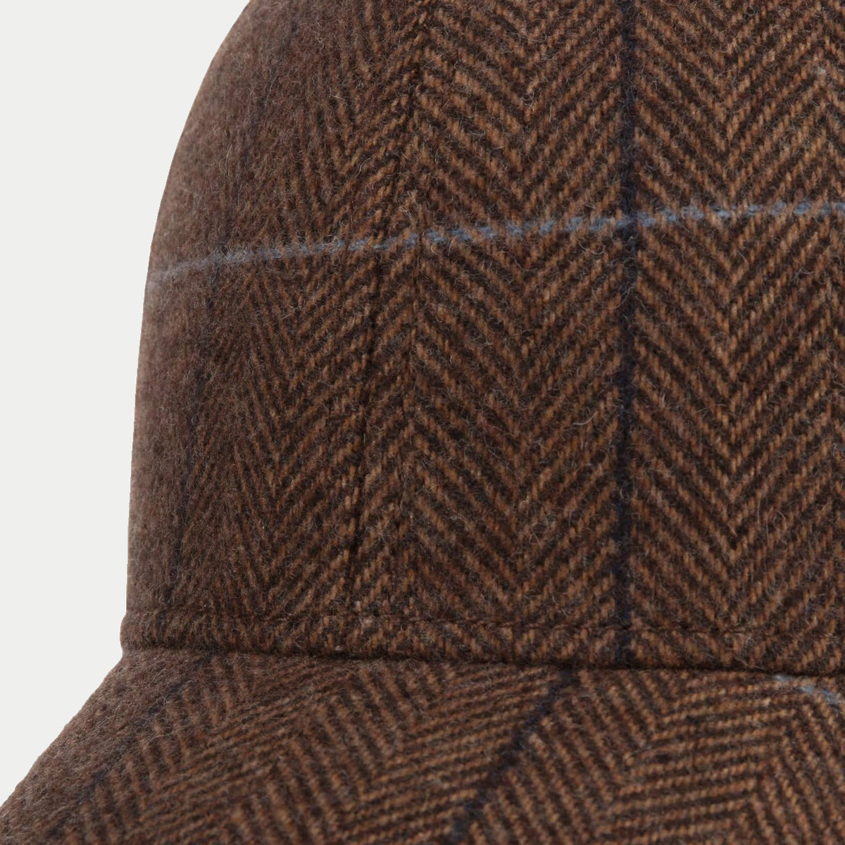 Gros plan sur la laine à chevrons marron et les carreaux bleu marine et bleu gris de la casquette Kinty