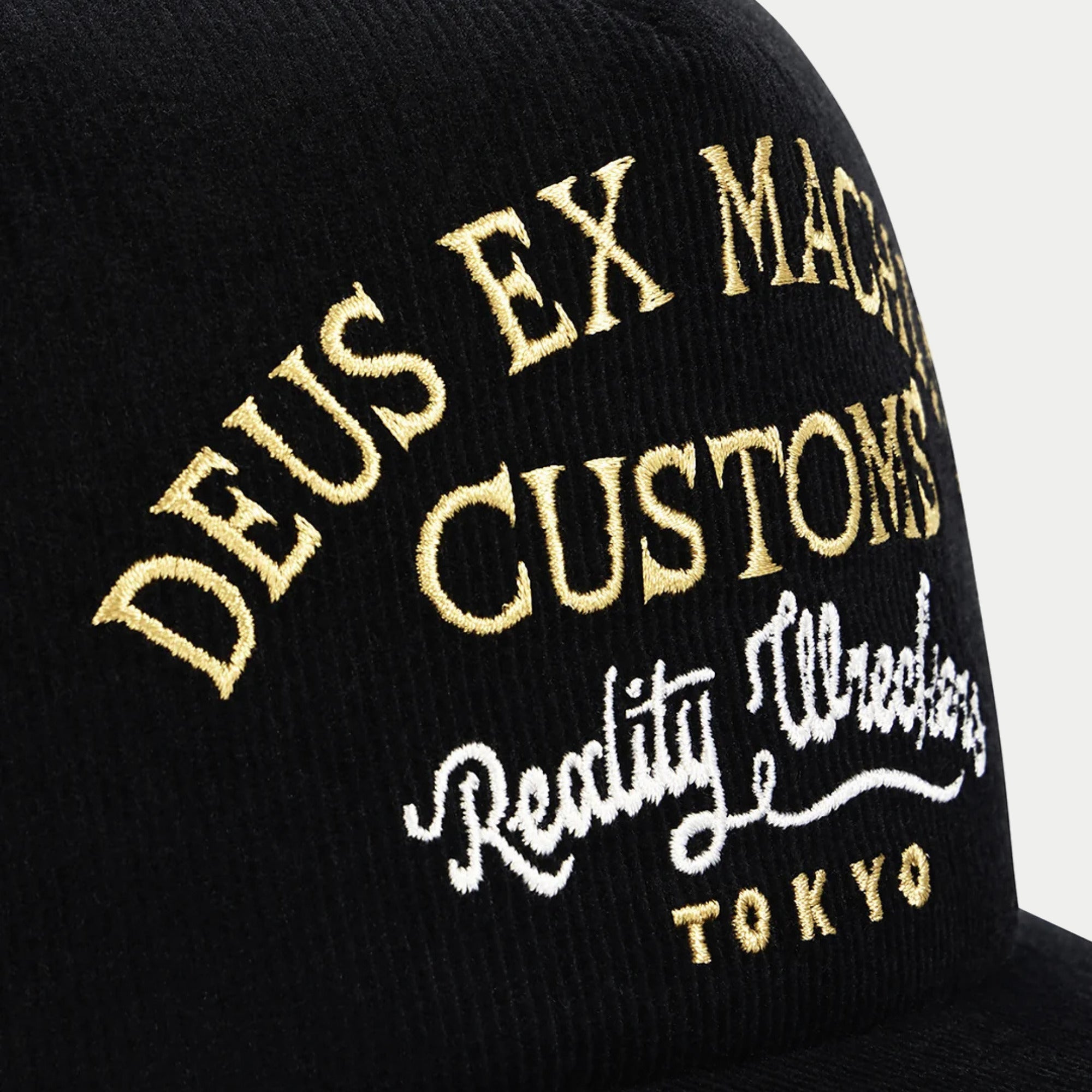 Gros plan des côtes du velours noir et de la broderie or blond et blanc Reality Wreckers Tokyo de la casquette Marsden