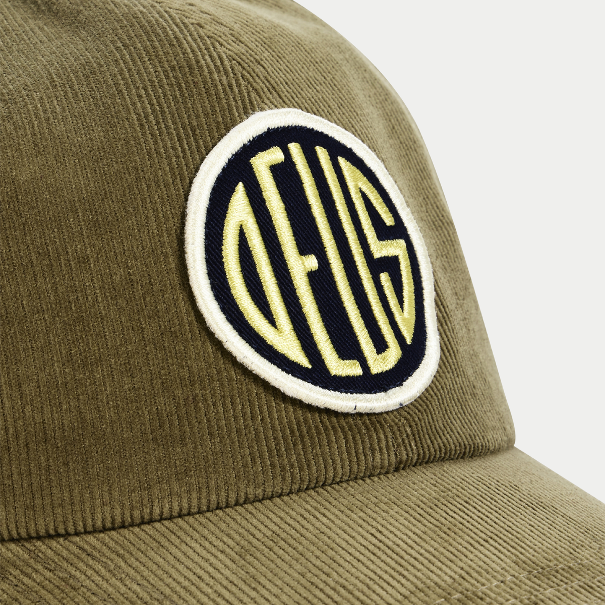 Casquette Pill Cord Olive Deus Ex Machina - gros plan du badge DEUS brodé jaune sur bleu marine