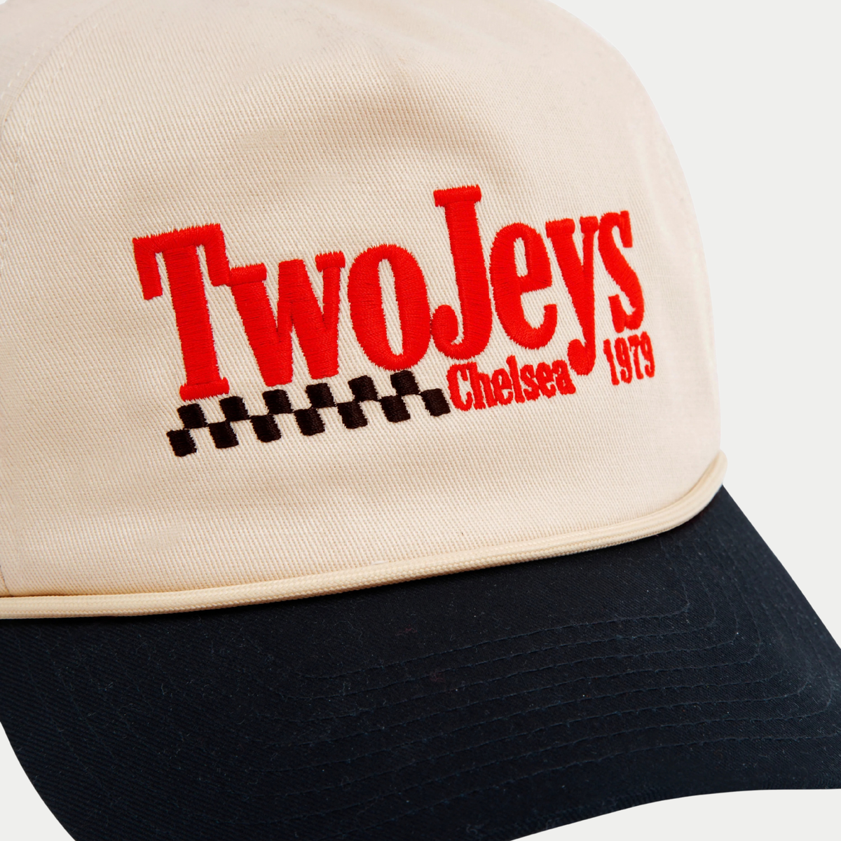 Gros plan sur la broderie TwoJeys Chelsea 1979 rouge et le damier noir de la casquette Racing