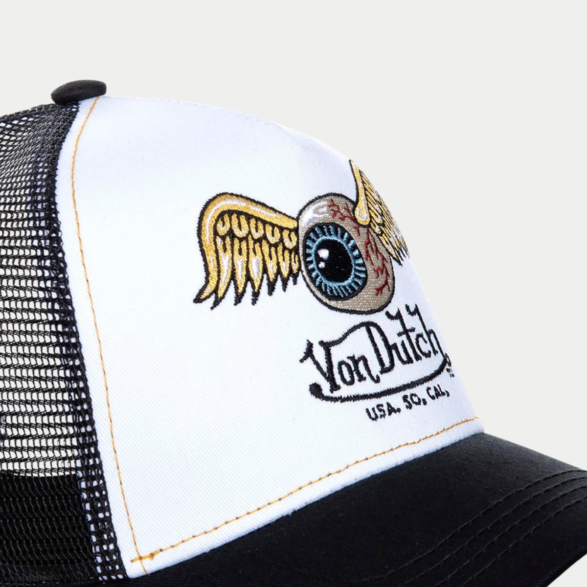 Gros plan de la broderie Flying Eye aux ailes dorées sur le panneau avant blanc de la casquette Von Dutch