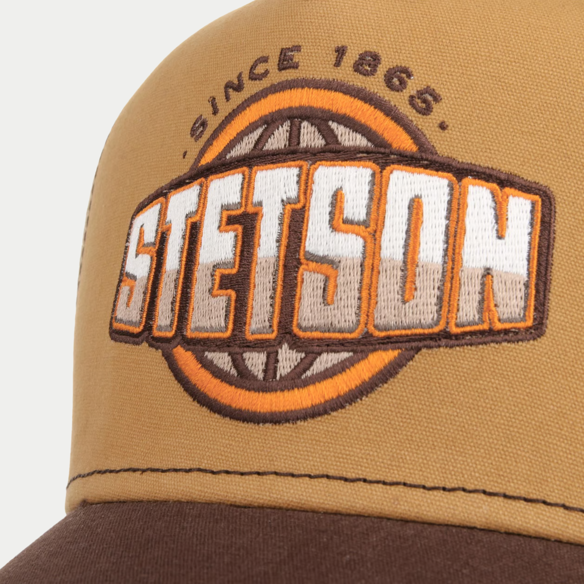 Gros plan sur l'écusson brodé Stetson Since 1865 au globe orange, sur le chino-twill camel de la casquette