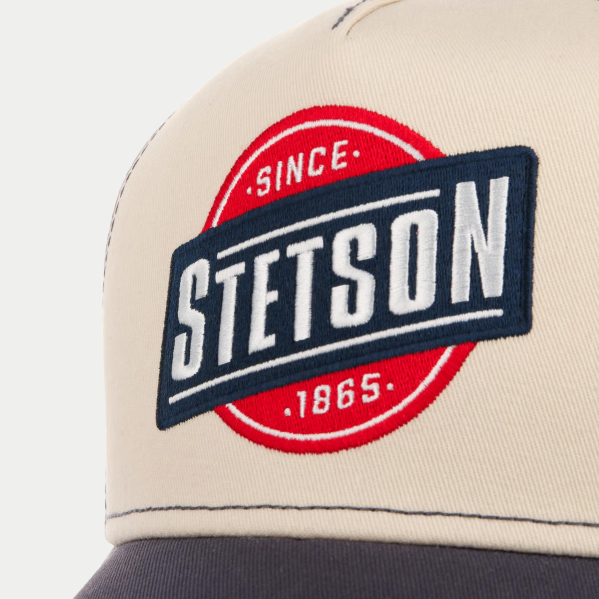 Gros plan de l'écusson brodé Stetson Since 1865 bleu marine, rouge et blanc sur le devant beige