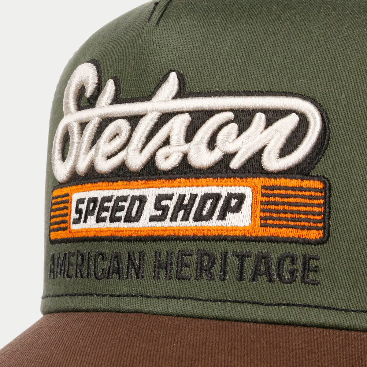 Gros plan sur la broderie Stetson Speed Shop, bandeau orange et lettrage American Heritage noir sur coton olive