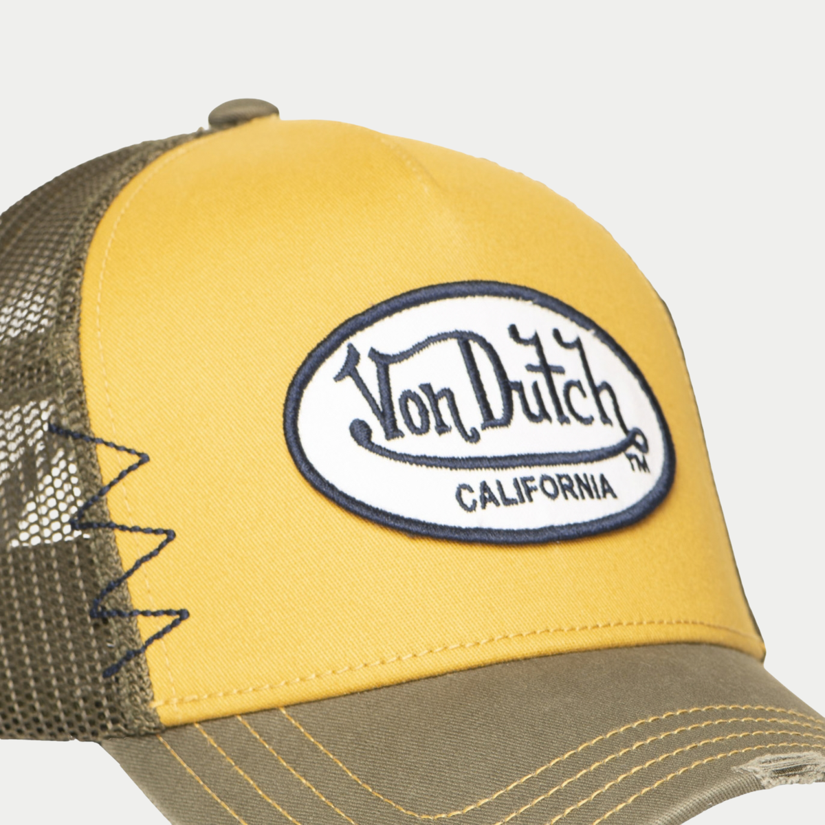 Gros plan sur l'écusson Von Dutch California brodé de la casquette trucker Used moutarde