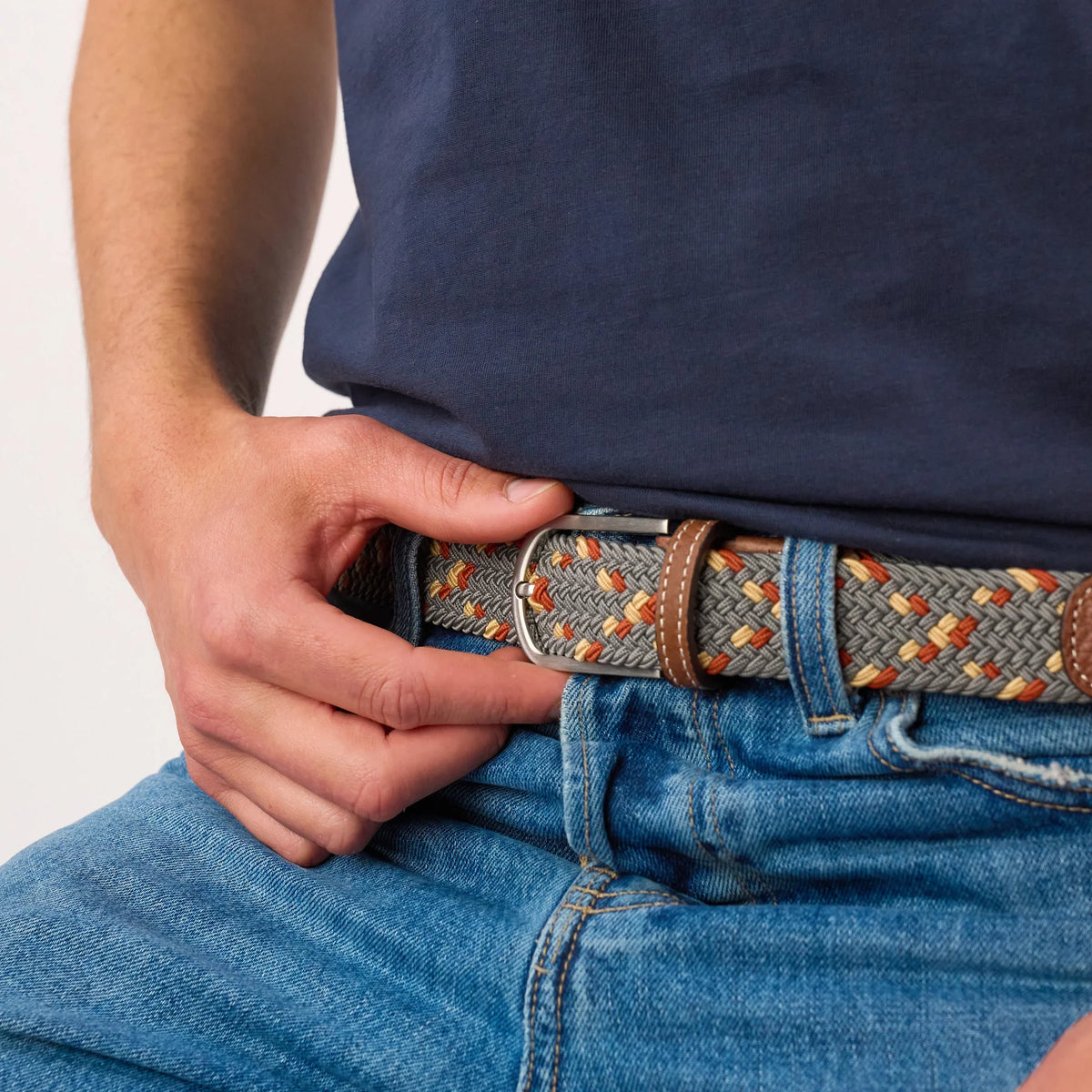 Gros plan de la ceinture Atacama portée sur un jean, boucle à ardillon argentée et passant en cuir sur la tresse grise et orange.