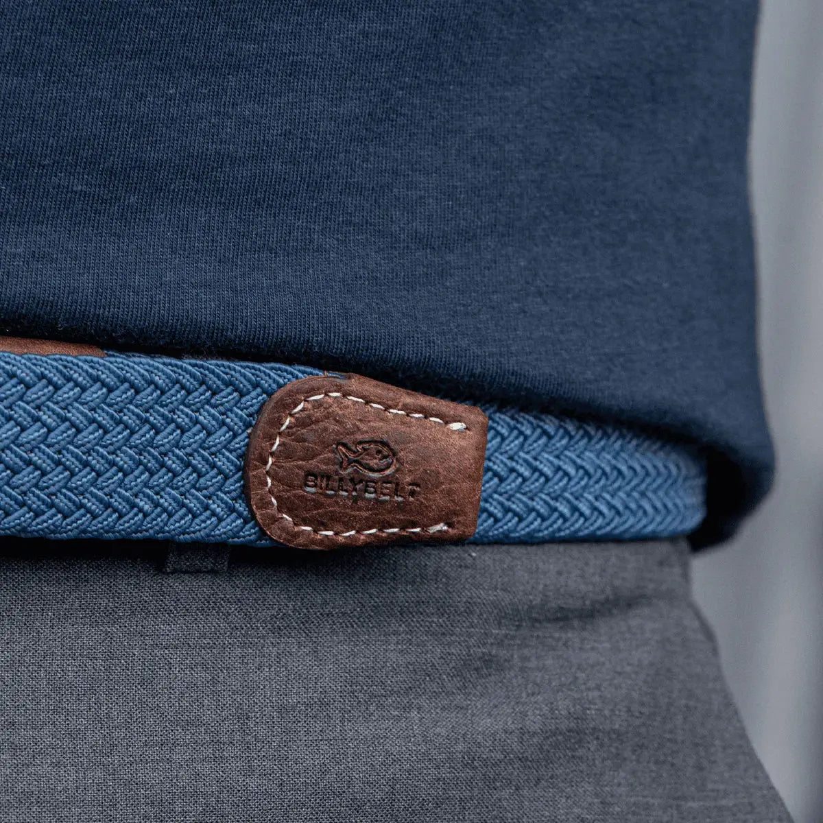 Patte de cuir brun grainé au poisson gravé, terminant la tresse bleu jean Bleu Air Force sur un pantalon gris