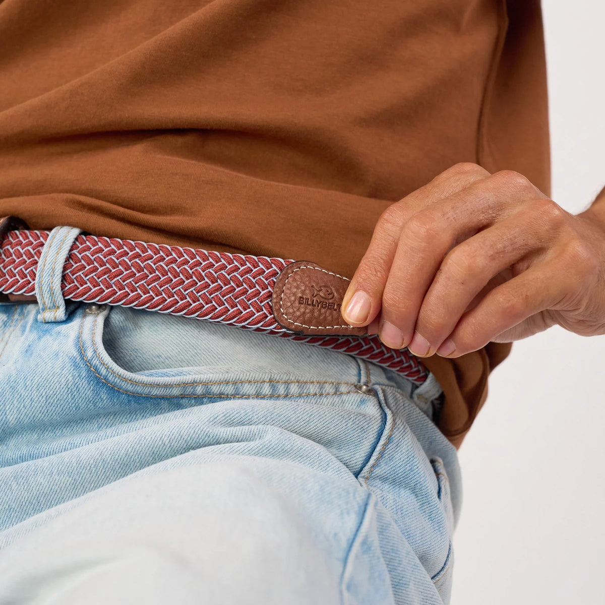 Embout en cuir marron au poisson estampé de la ceinture Sienne, tresse rouge brique et bleu ciel passée sur un jean clair