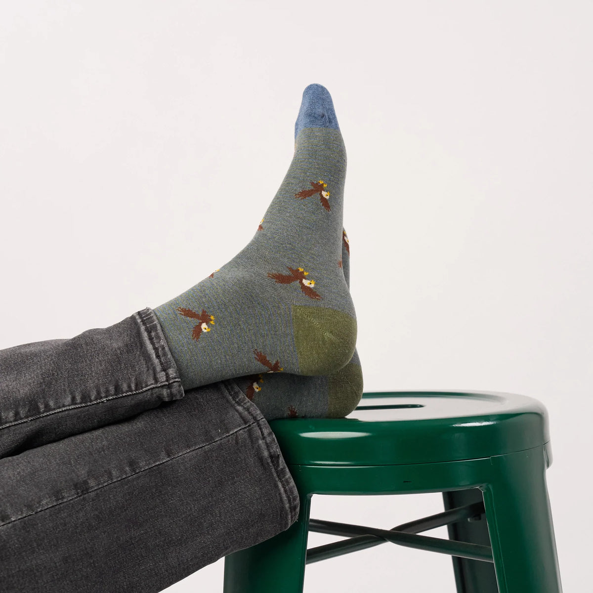 Chaussettes à motif aigles BillyBelt vues de dos, pointe bleue et talon vert olive sur un tabouret