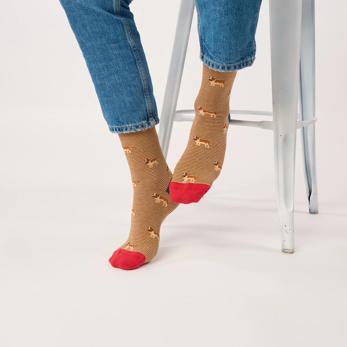 Chaussettes Saint-Bernard BillyBelt portées sous un jean retroussé, pieds croisés près d'un tabouret blanc