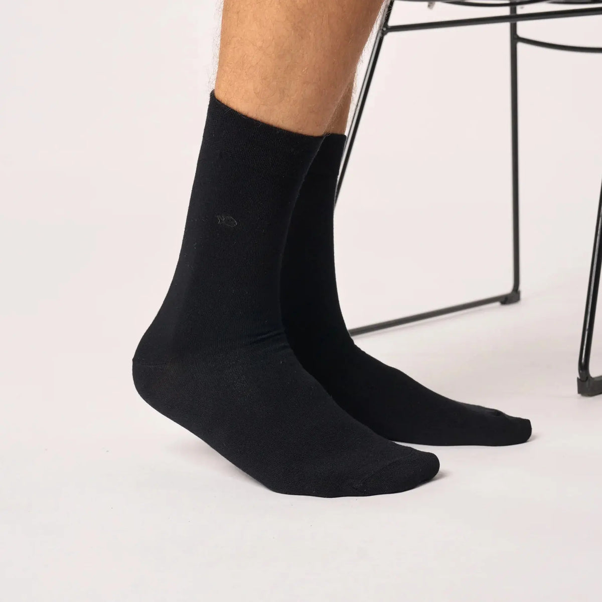 Paire noire en bambou portée de trois quarts, tige droite et maille unie, devant un fauteuil en fil noir