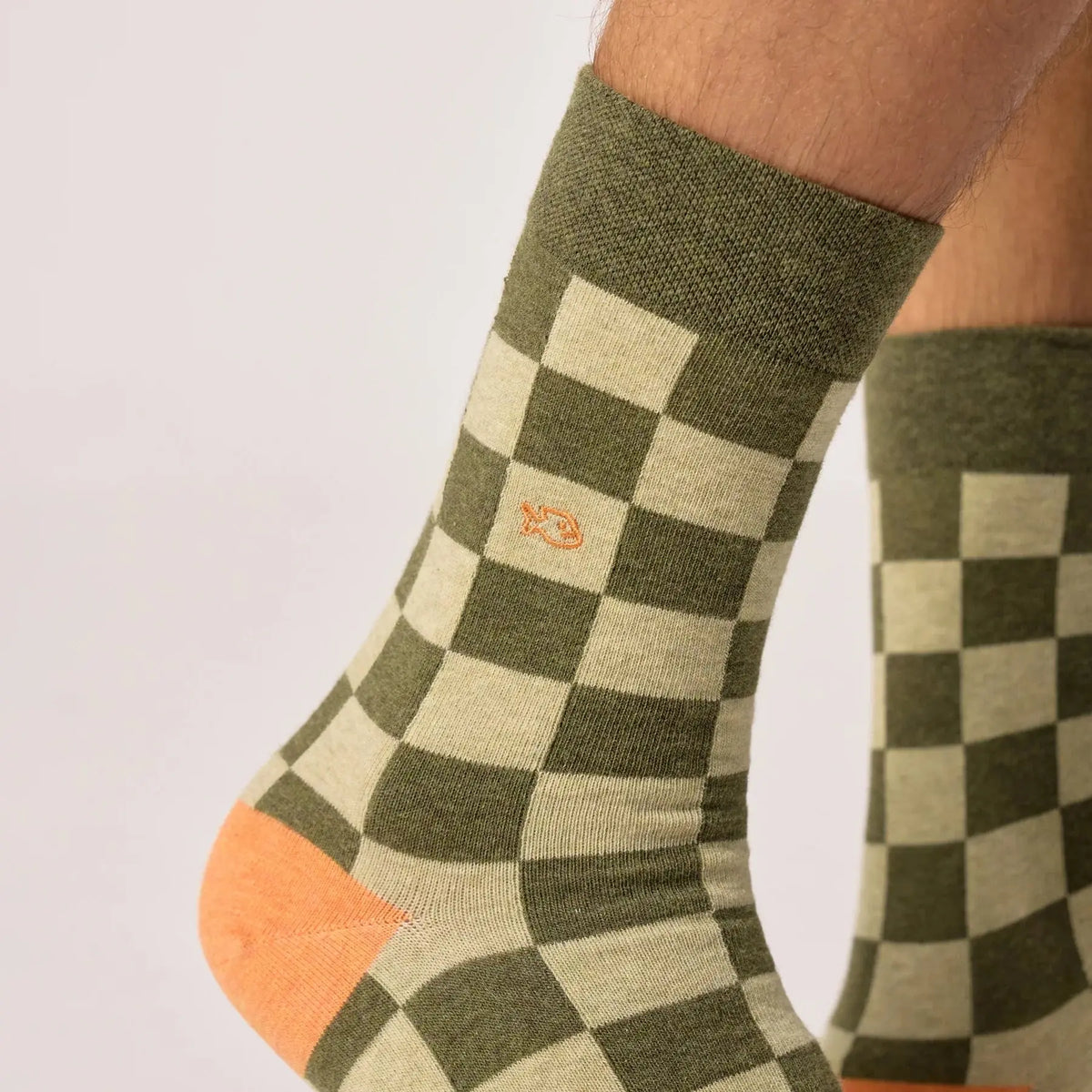Gros plan du damier kaki et vert clair, du poisson orange brodé et du talon orange des chaussettes Boavista