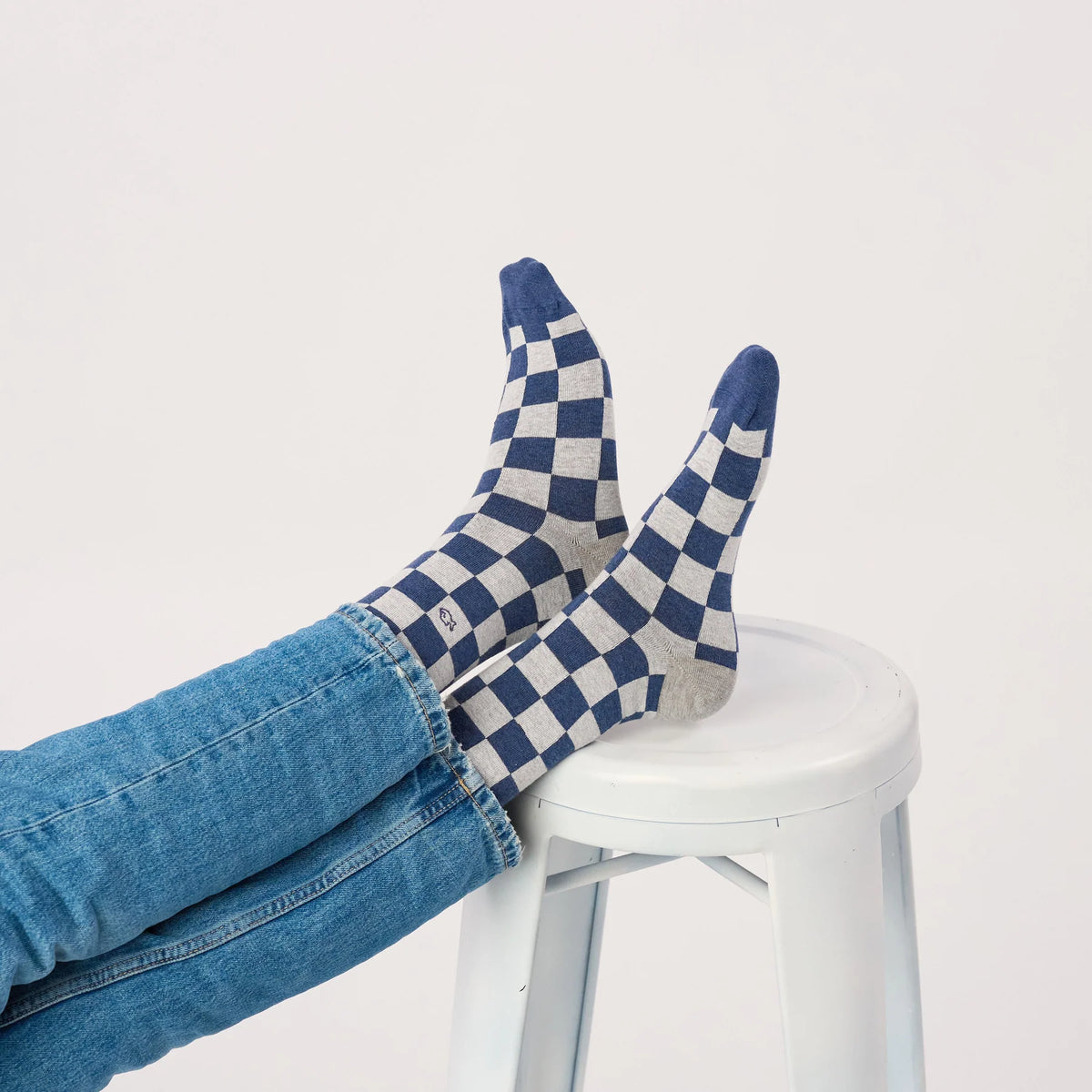 Chaussettes à carreaux bleus et gris portées, pieds posés sur un tabouret blanc, pointes bleues