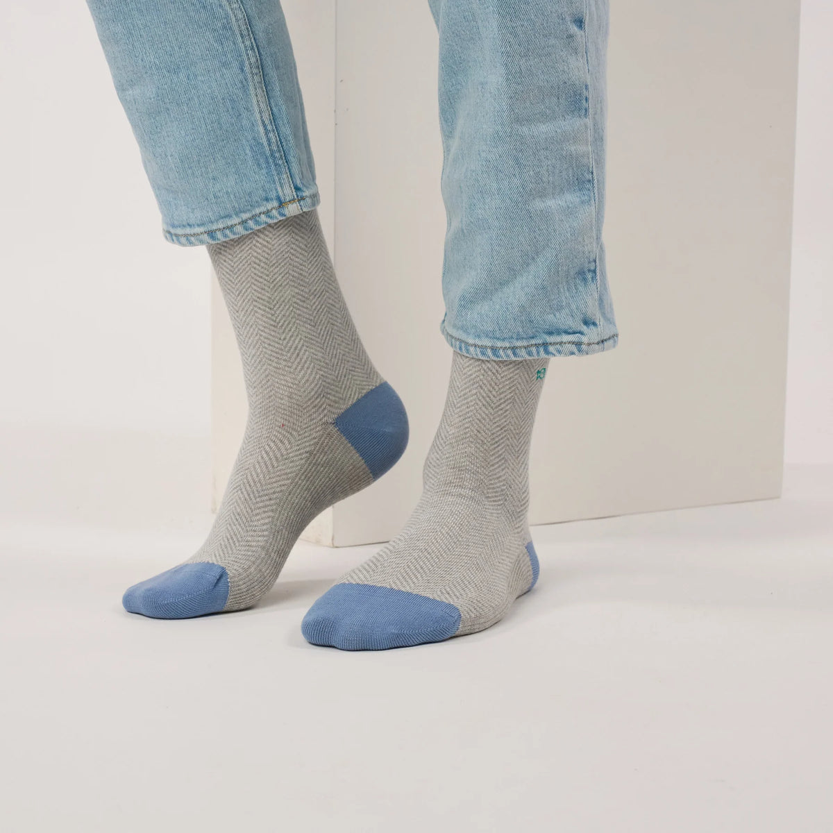 Paire de chaussettes à chevrons gris cendré vue de face, talons et pointes bleu ciel sous un jean clair