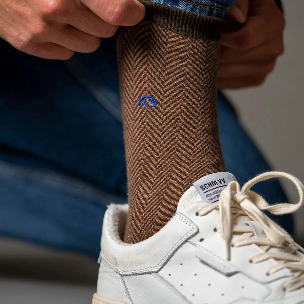 Chaussette à chevrons marron enfilée sous un jean dans une basket blanche, petit poisson brodé bleu roi sur la tige