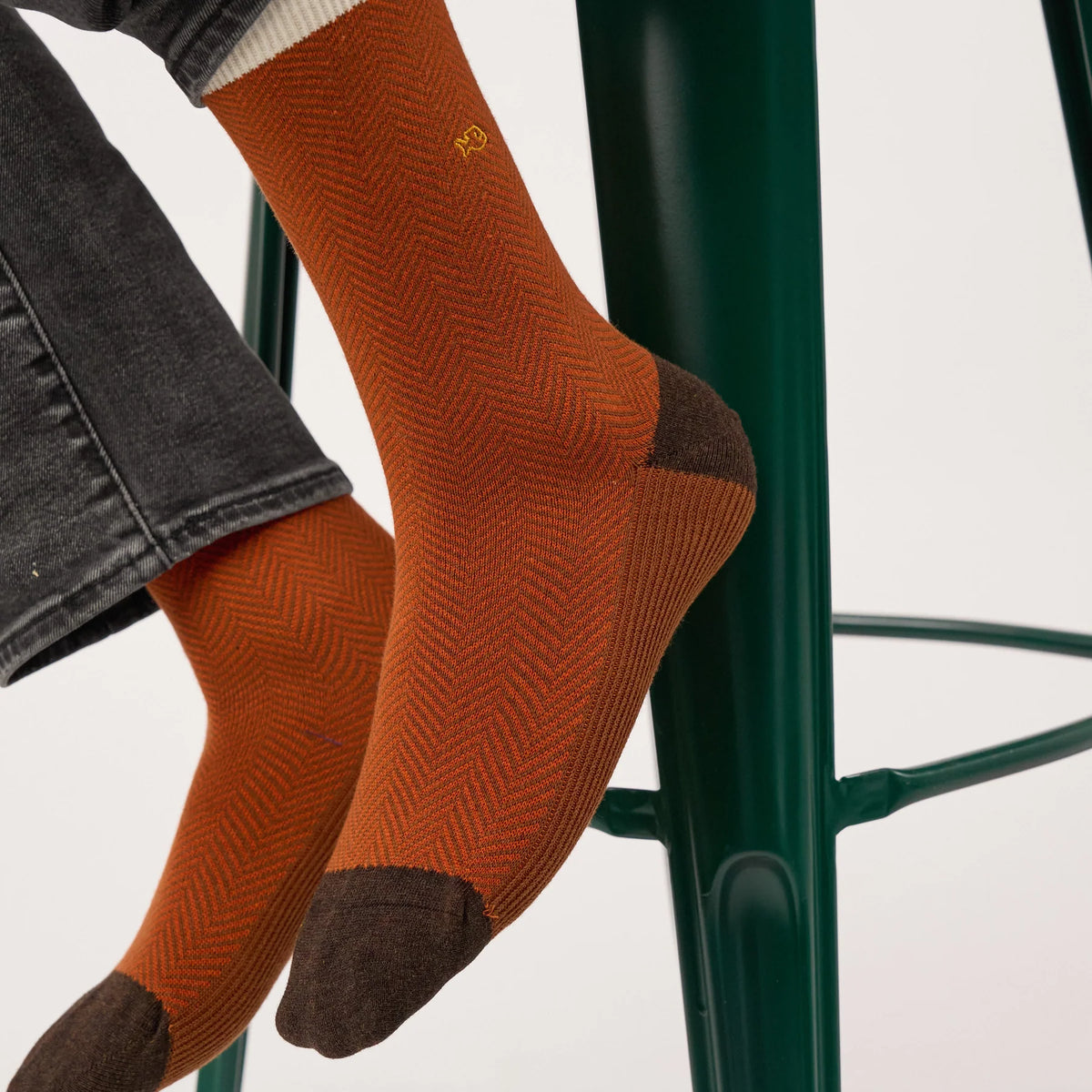 Gros plan des chaussettes Chevrons Sépia portées : tissage chevrons rouge brique et logo brodé jaune