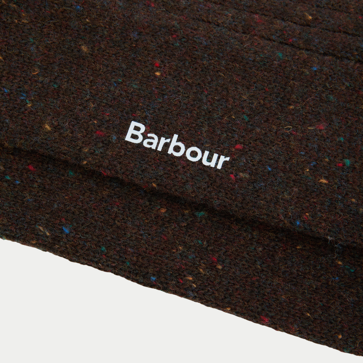 Macro de la laine brun chocolat semée de neps rouges, bleus et jaunes, logo Barbour blanc sur la tige.