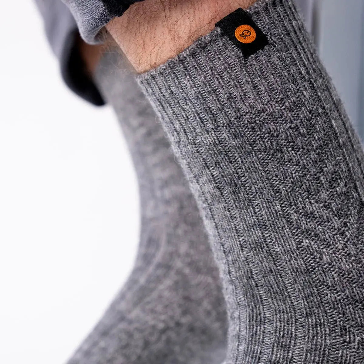 Macro de la laine gris chiné : côtes en relief, damier tricoté et étiquette noire au logo orange sur le bord