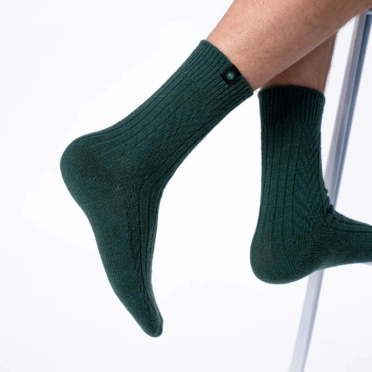 Chaussettes en laine vert sapin portées pieds relevés, les côtes courent de la tige à la pointe arrondie