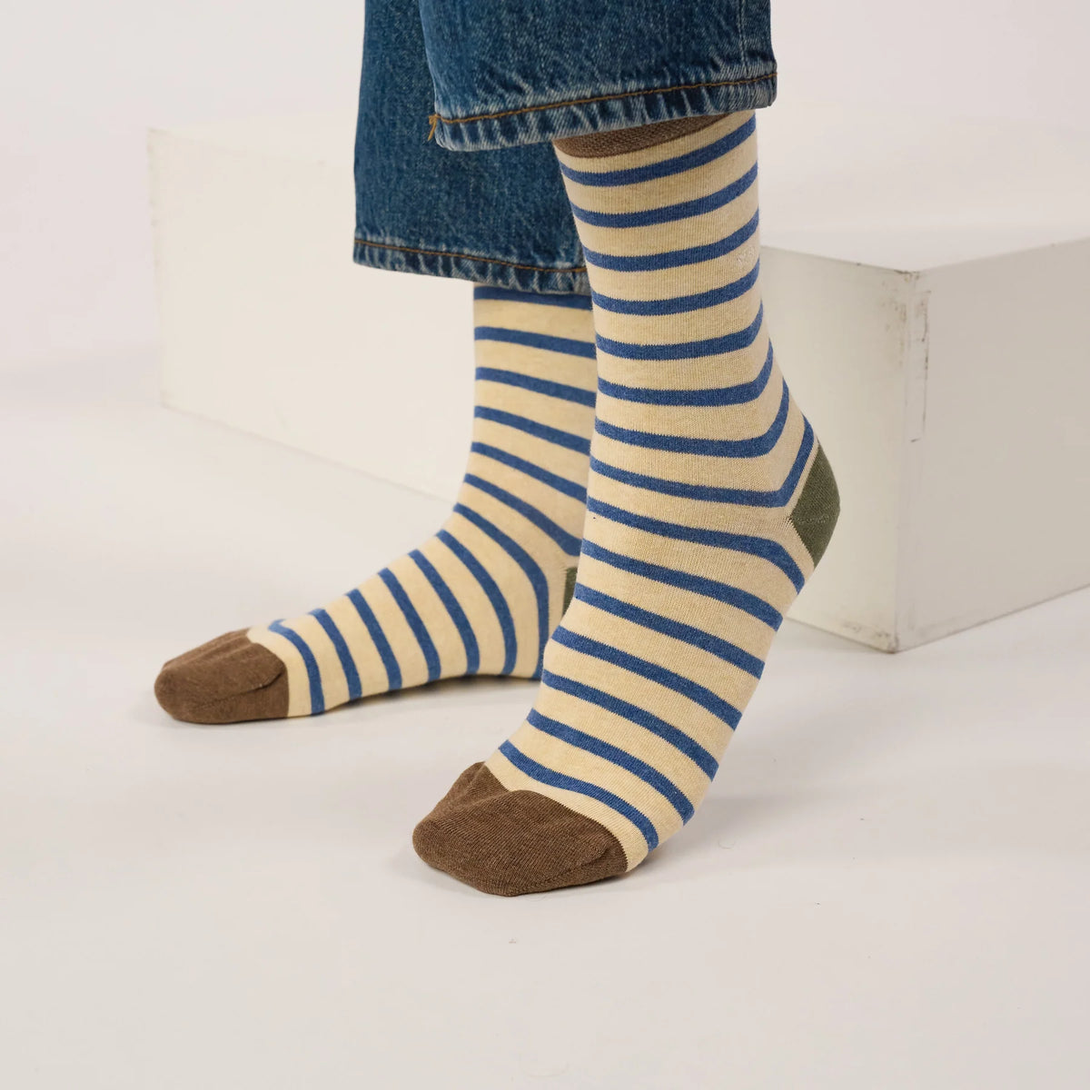 Paire de chaussettes rayées beige et bleu portées sous un jean, pointes marron et talon kaki visibles.