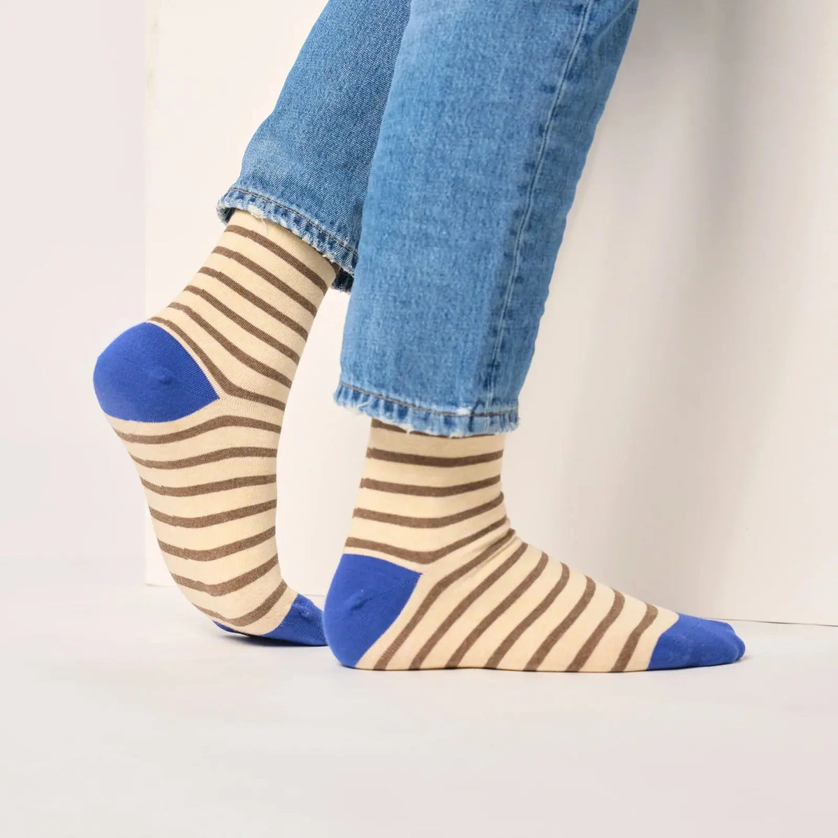 Vue de profil des chaussettes beige à rayures marron portées, talon bleu roi sur un pied levé.